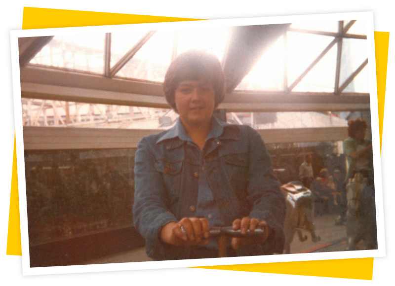 A young, teenage Tony rides on a carousel, while wearing double-denim and a blue wide-collared shirt. Late 1970s. Image donated by Tony Wright.